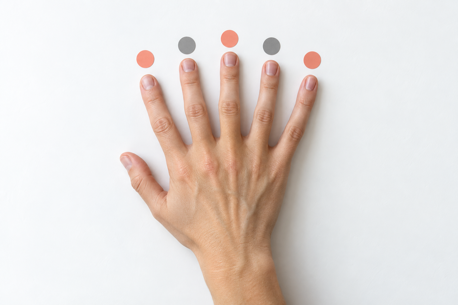 One complete adult hand rests above five alternating coral and gray practice markers on a white surface